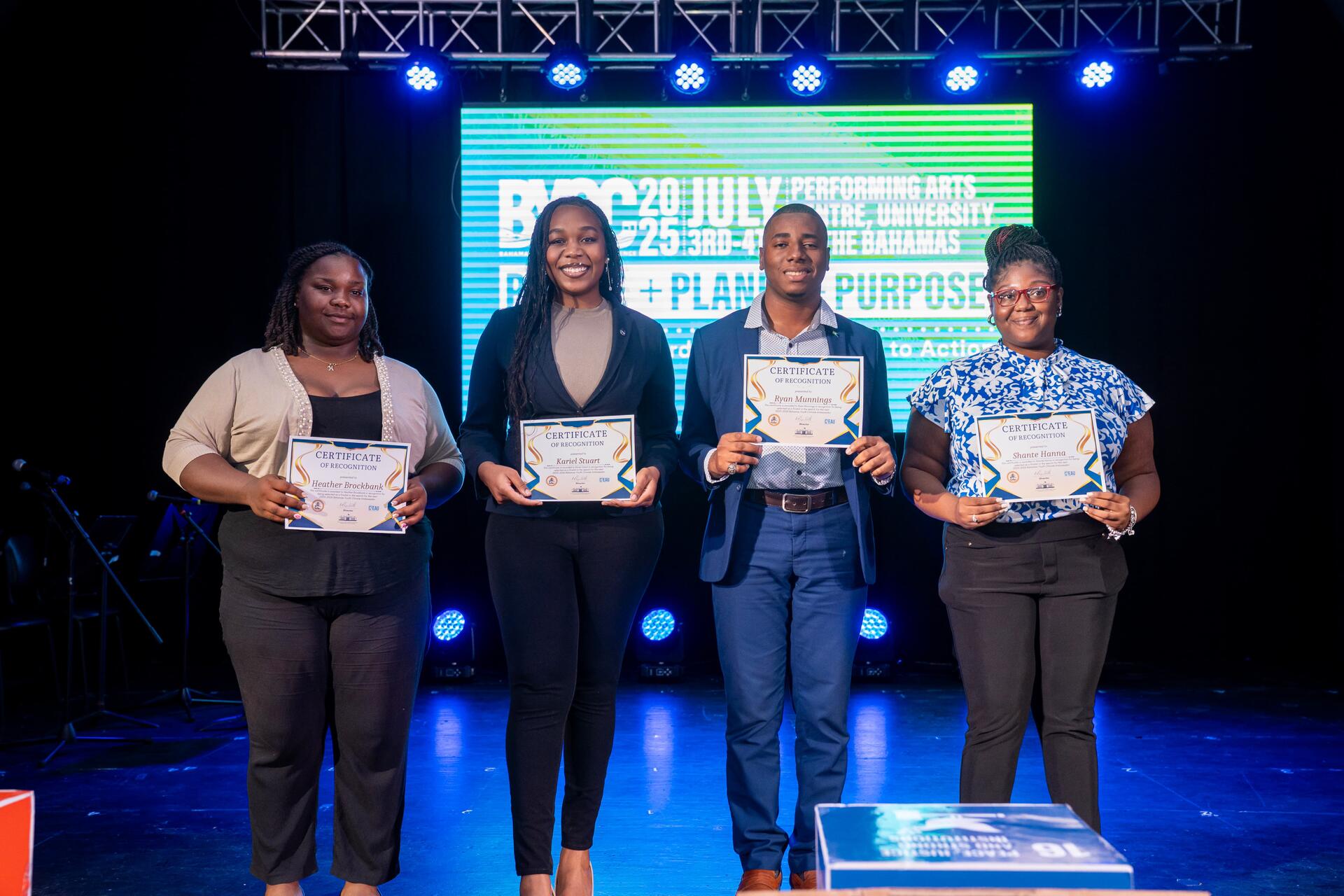 Kariel and three fellow committee members holding certificates of recognition on stage